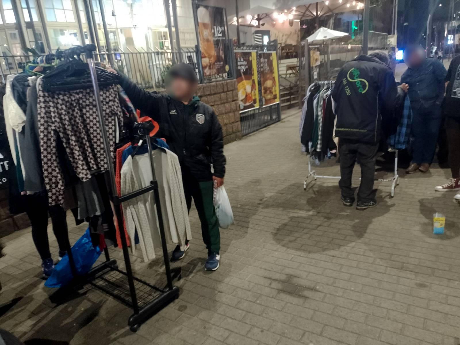 Foto de pessoas olhando e experimentando roupas em uma praça.