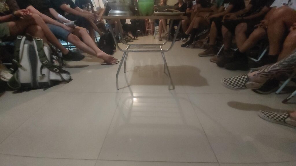 Foto mostra as pernas de diversas pessoas sentadas em círculo.